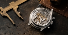 Ein schlankes 41 mm Breitling-Uhrgehäuse aus gebürstetem Edelstahl liegt auf einer dunklen Werkbank, der Saphirglasboden