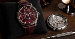 Ein burgunderroter Frederique Constant Classic Perpetual Calendar liegt auf einem schwarzen Kissen neben einem offenen
