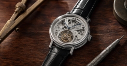 Eine offene Breguet Classique Tourbillon Uhr mit detailliertem Uhrwerk liegt auf dunklem Holz, daneben liegen ein antiker