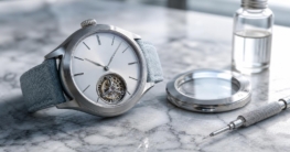 Eine luxuriöse Uhr mit silbernem Gehäuse und opalweißem Zifferblatt liegt auf einem marmornen Tisch neben einem
