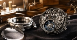 Makroaufnahme eines offenen Luxus-Uhrwerks mit blau-DLC-beschichtetem Tourbillon auf dunklem Samt, daneben Uhrgehäuse und