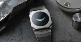 Eine achteckige, ultraflache Uhr mit gebürstetem Edelstahlgehäuse auf einem rauen, betonierten Hintergrund, begleitet von