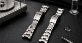 Zwei glänzende Armbänder aus Titan und Edelstahl liegen nebeneinander auf einer schwarzen Oberfläche mit einem Messzylinder